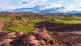 Aerial landscape view of rolling green fields with rocky outcrops and mountains under cloudy sky