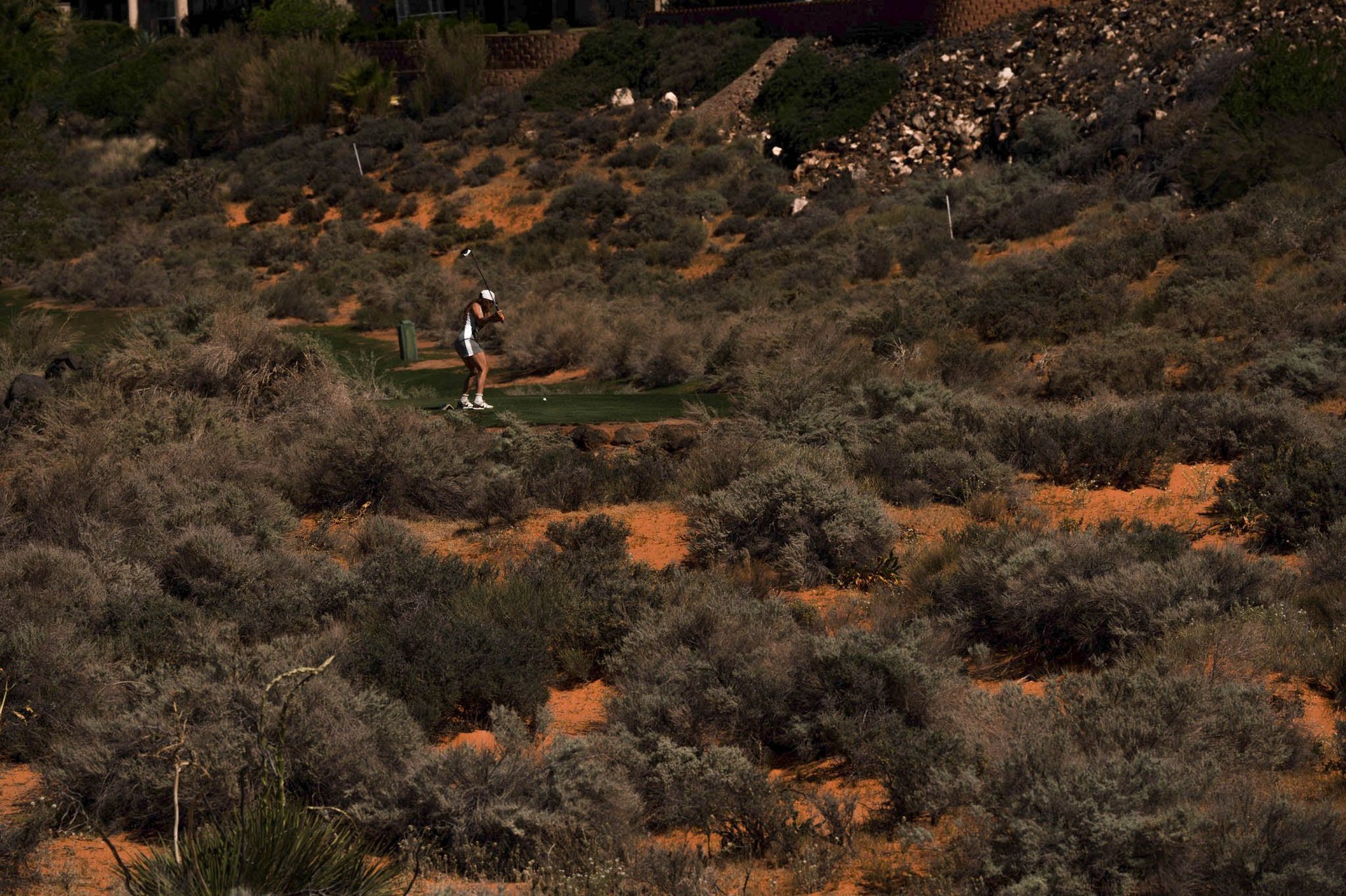 Runner jogging on trail through arid hillside with sparse desert shrubs and orange-brown soil
