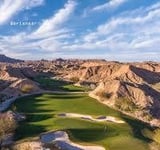 Aerial view of a desert golf course with green fairway surrounded by rugged brown cliffs and rocks